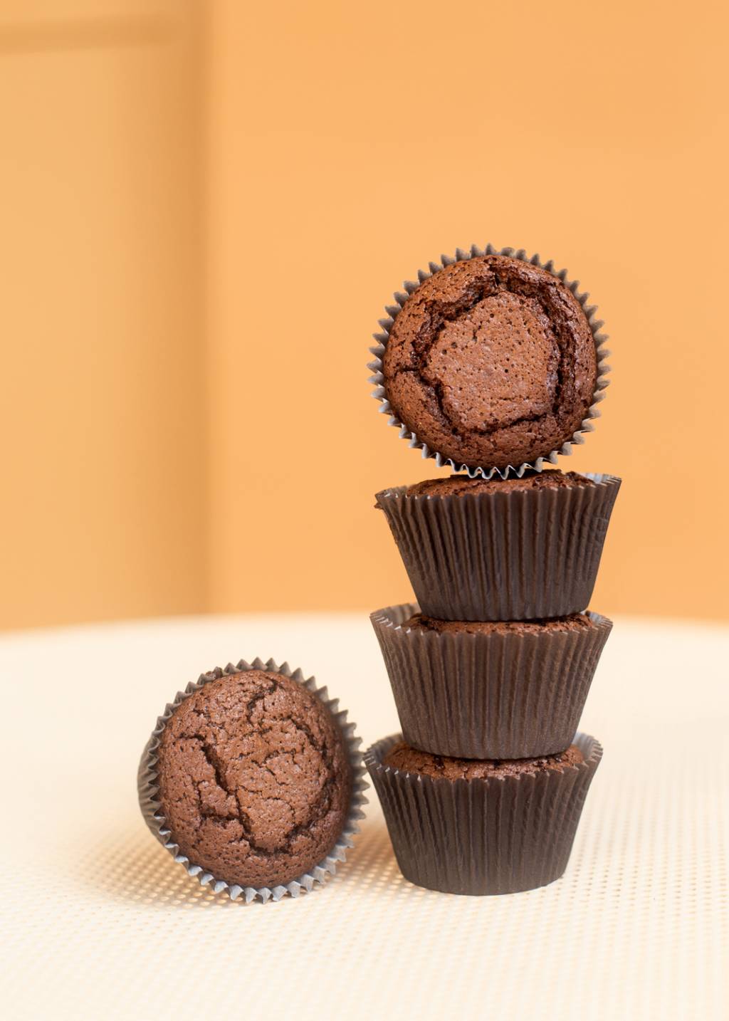 Quatro brownies de chocolate em forminhas empilhados ao lado de outro brownie.
