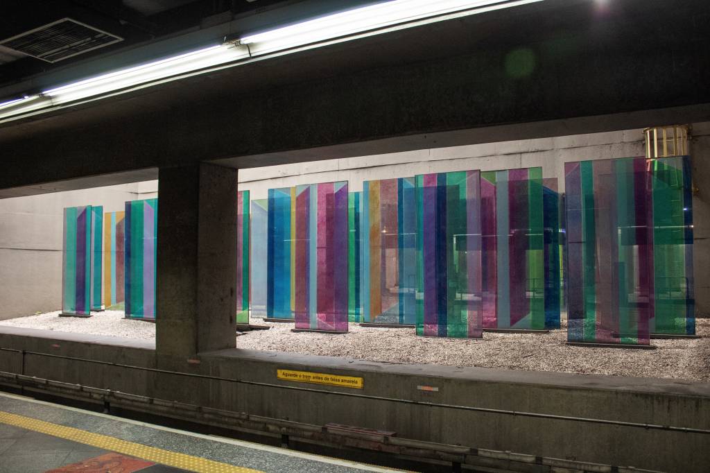 Instalação de vidros retangulares expostos em vão de metrô, atrás dos trilhos