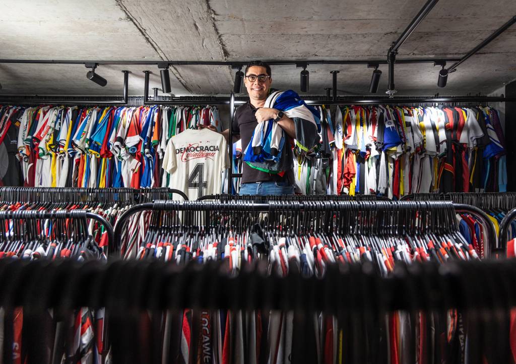 CASSIOCOLECCAMISAS11 Homem posa no meio de araras e cabides repletos de camisas de futebol
