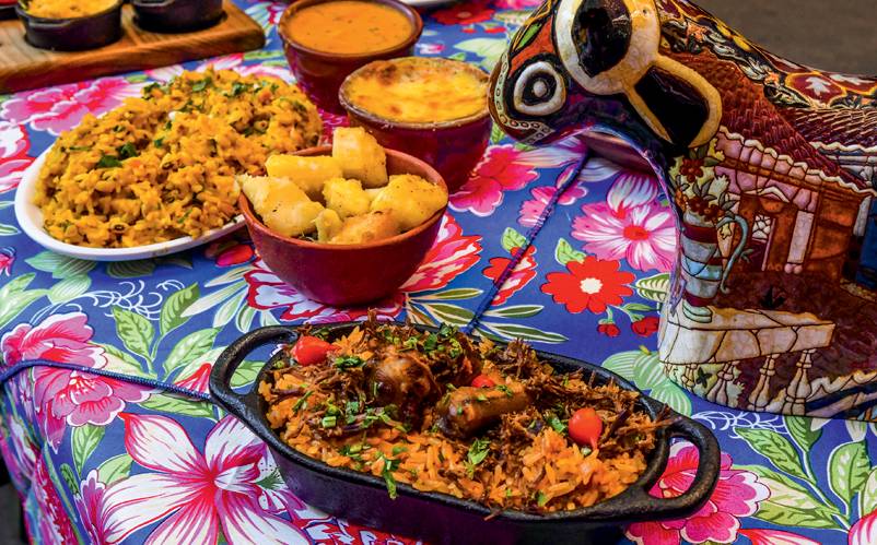 Festa Junina – Centro de Tradições Nordestinas Mesa com toalha florida com comidas juninas em cumbucas.