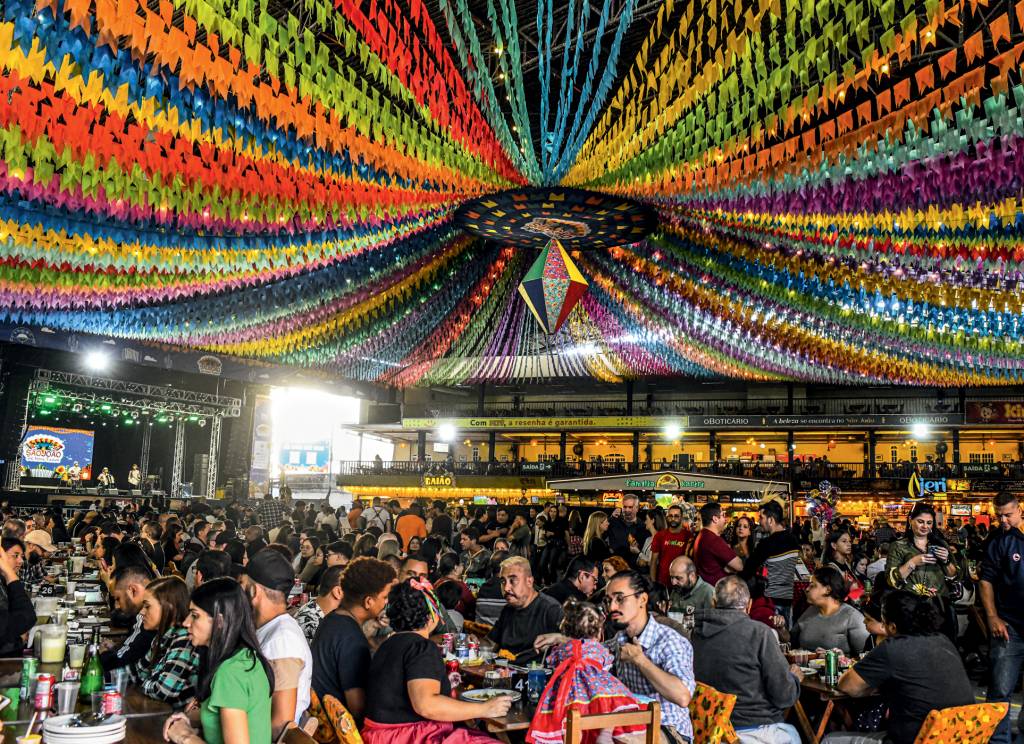 Festa Junina do Centro de Tradições Nordestinas com bandeirinhas coloridas no teto e pessoas sentadas em mesas no salão