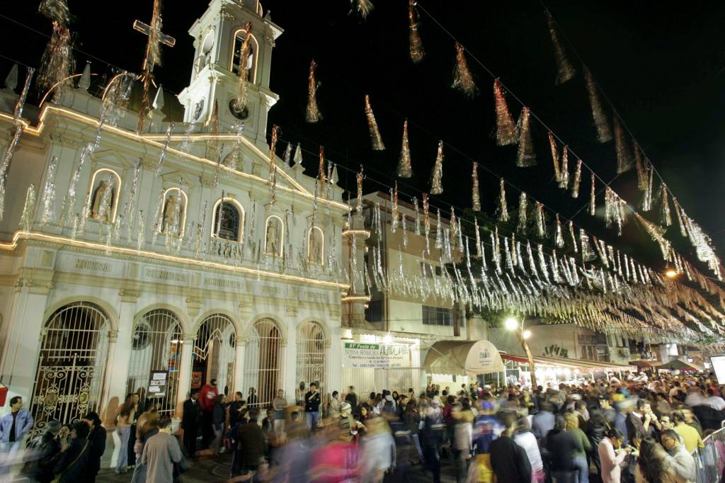Festa Junina – Achiropita Igreja Achiropita à esquerda, com público na frente e bandeiras penduras por cima.