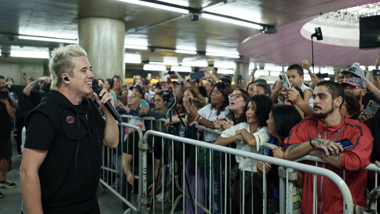 Vocalista da banda Jota Quest canta em frente a grade de metrô com multidão à direita