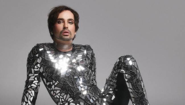 Johnny Hooker posa de perna flexionada em macacão prateado