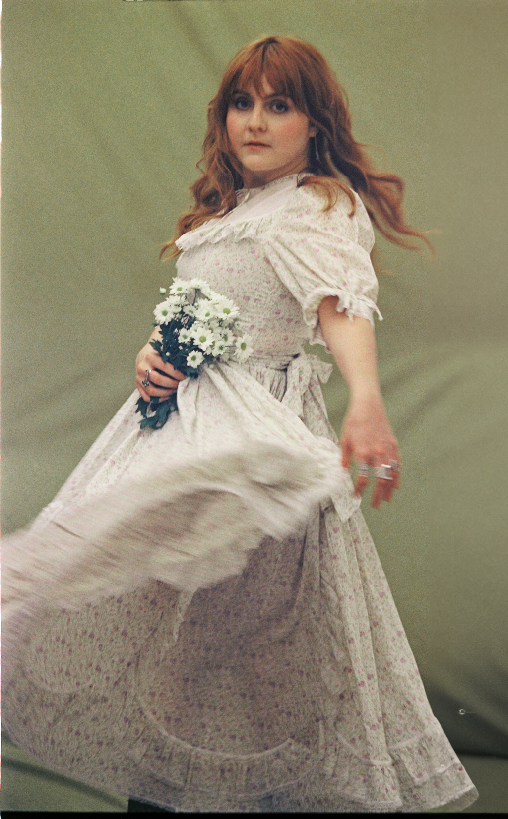 Mulher ruiva posa com buquê de flores brancas na mão vestindo vestido branco com a saia em movimento