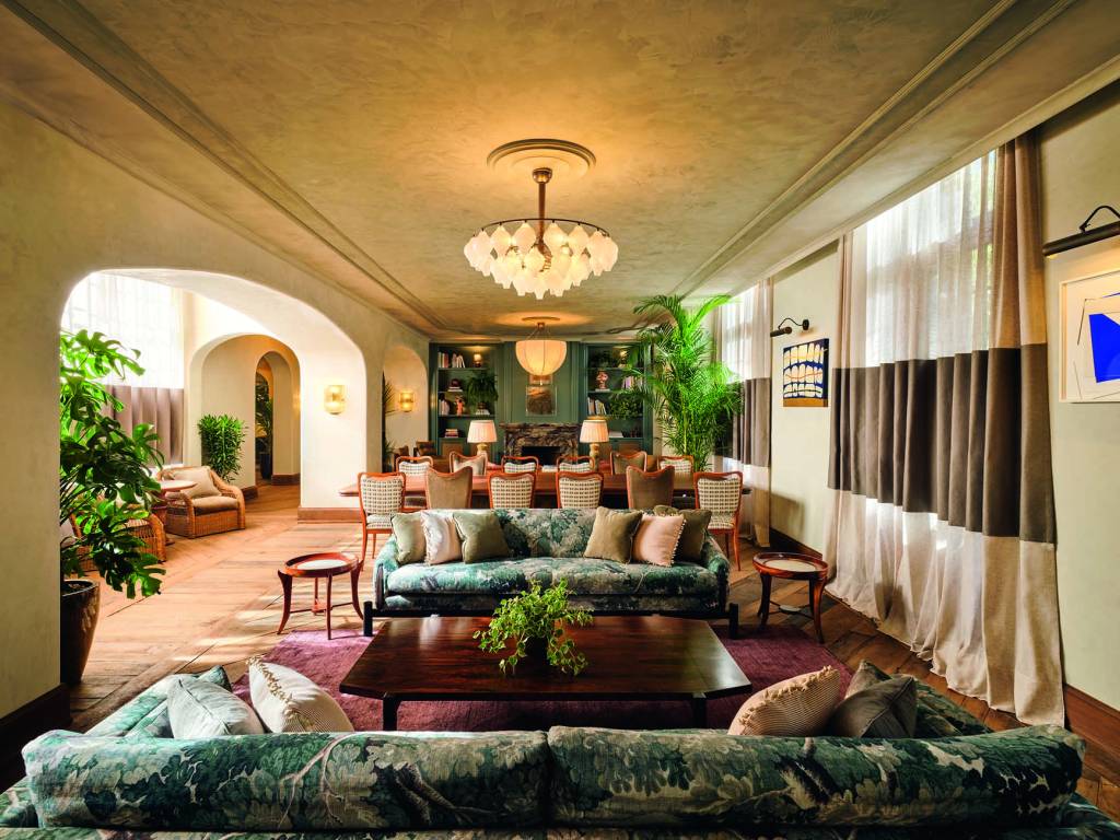 Foto de ambiente mostra sofás, lustre e mesas com arco à esquerda