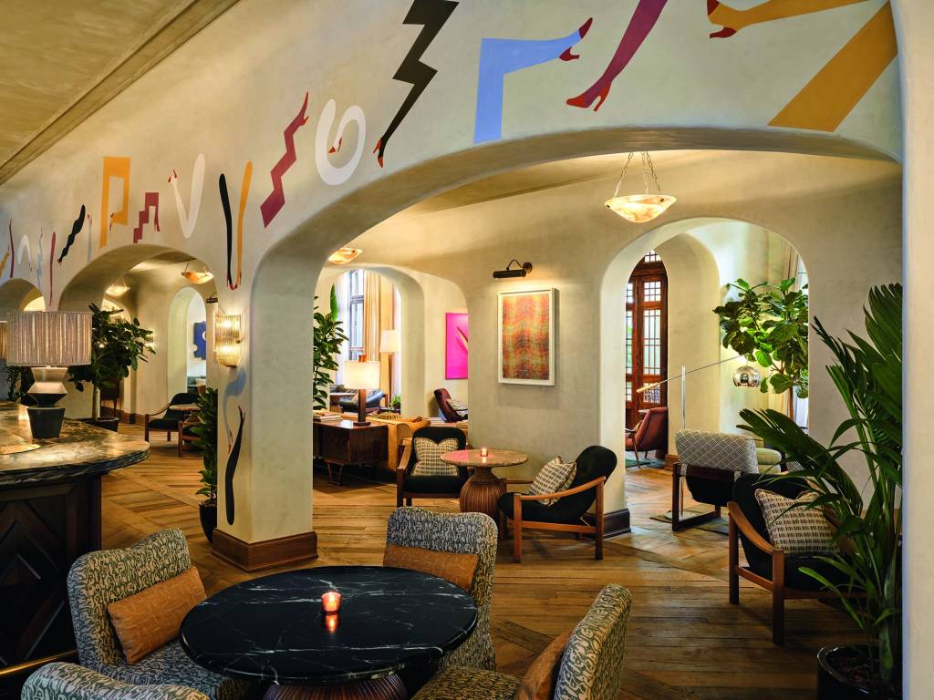 Soho House São Paulo-Crédito Soho House-Divulgação (4) Foto de ambiente mostra arco com pintura artística e ambiente de mesas, cadeiras e poltronas