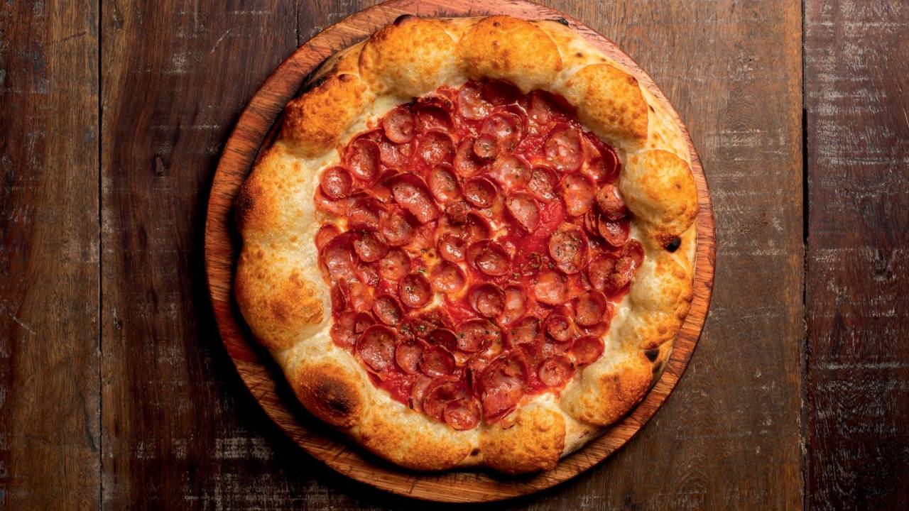 Foto aérea de pizza de calabresa sobre tampo de madeira.