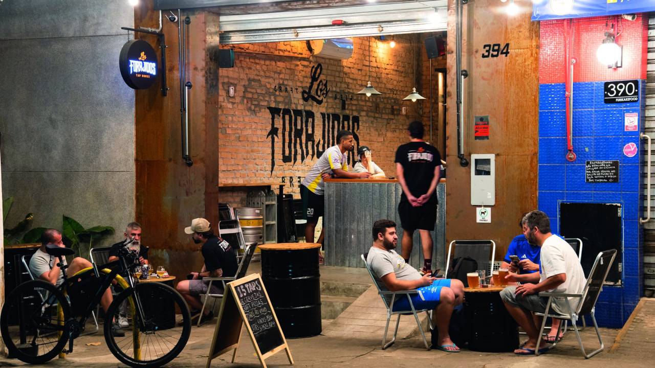 Fachada da cervejaria Los Forajidos com pessoas sentadas em mesinhas dobráveis na calçada.