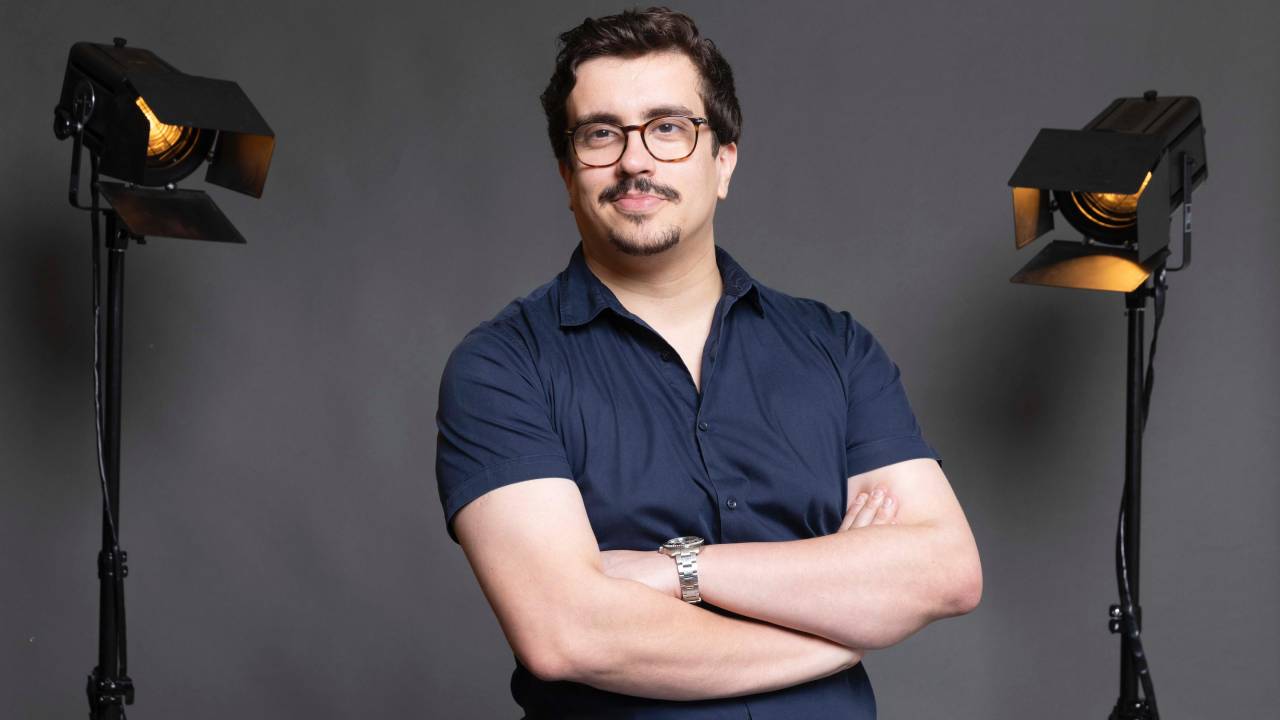 Homem branco de óculos posa de braços cruzados