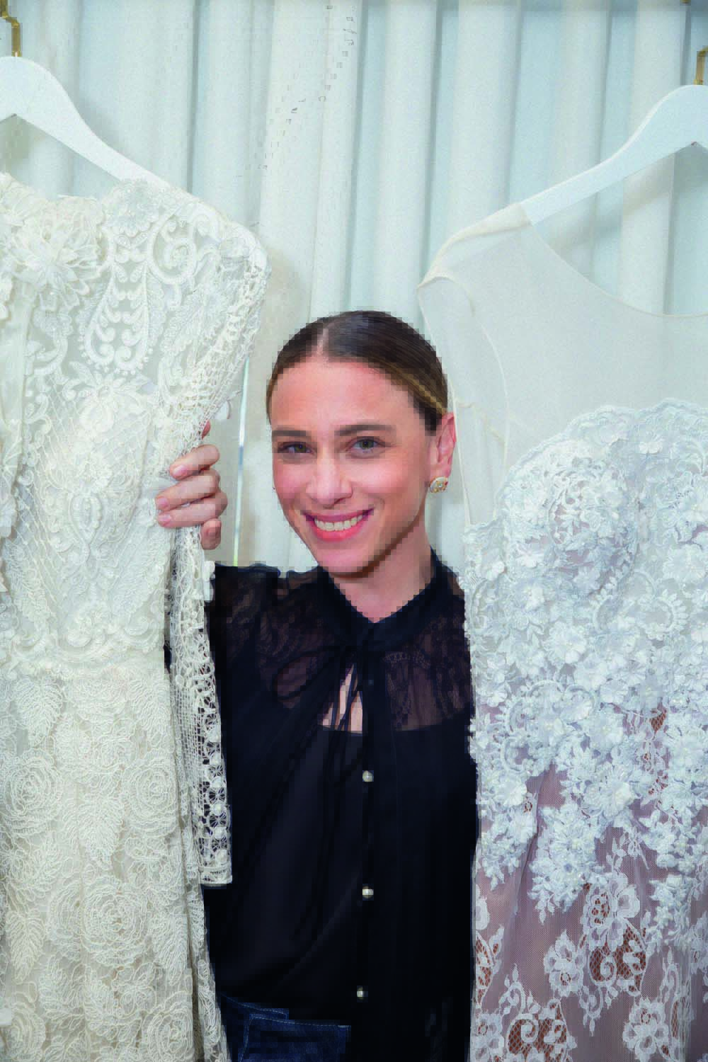 Lethicia Bronstein Crédito Wellington Marques-Divulgação (1).jpg Mulher loira sorri entre dois vestidos de noiva