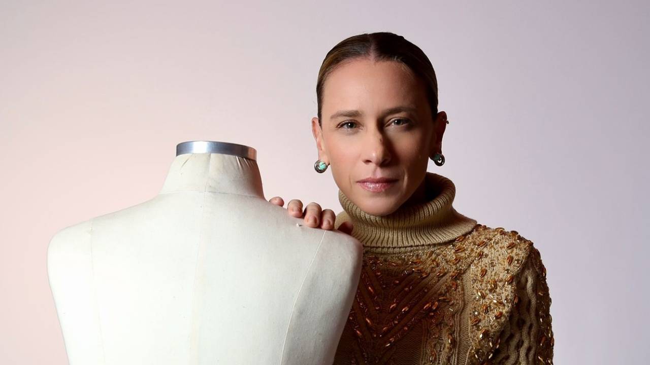Mulher loira posa séria ao lado de manequim branco e veste suéter marrom claro