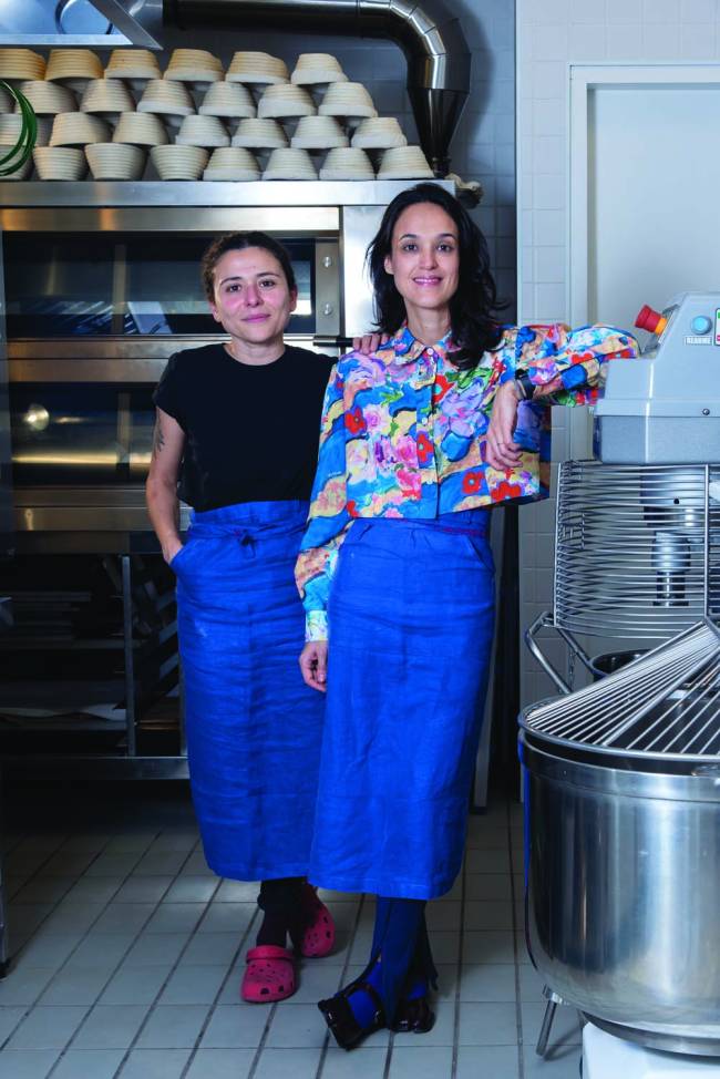 Duas mulheres na cozinha em pé e sorrindo