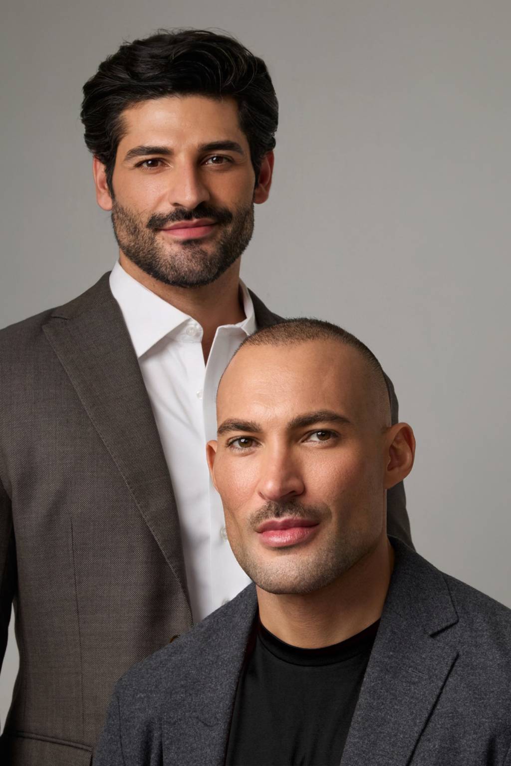 Romeu e Henrique, ROM Concept Crédito Henri Parv-Divulgação (2) Homem de barba e cabelos negros posa de pé ao lado de homem branco e careca, ambos sorrindo e vestindo ternos escuros.