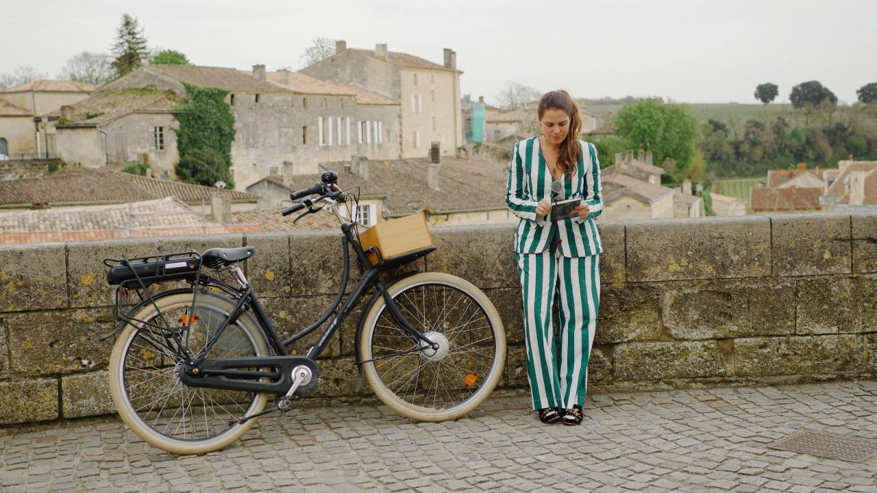 Moça loira encostada em muro com bike ao lado, veste peça listrada em branco e verde