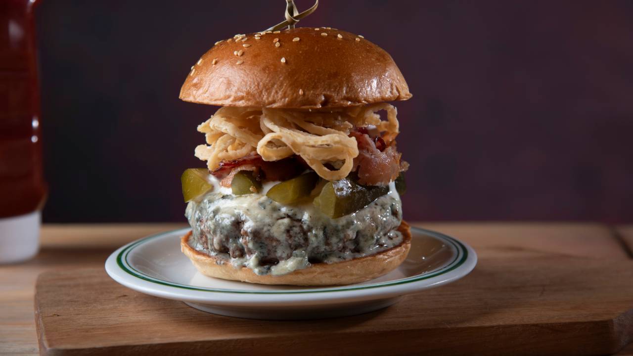 Hambúrguer com queijo gorgonzola e cebola crispy no prato em cima da mesa de madeira