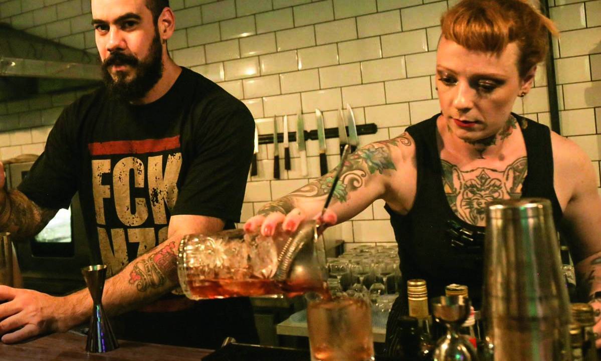 Duas pessoas fazendo drinques uma ao lado da outra