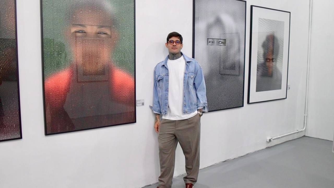 Gabriel Ferreira, fotógrafo documental, posa no meio de duas grandes fotografias