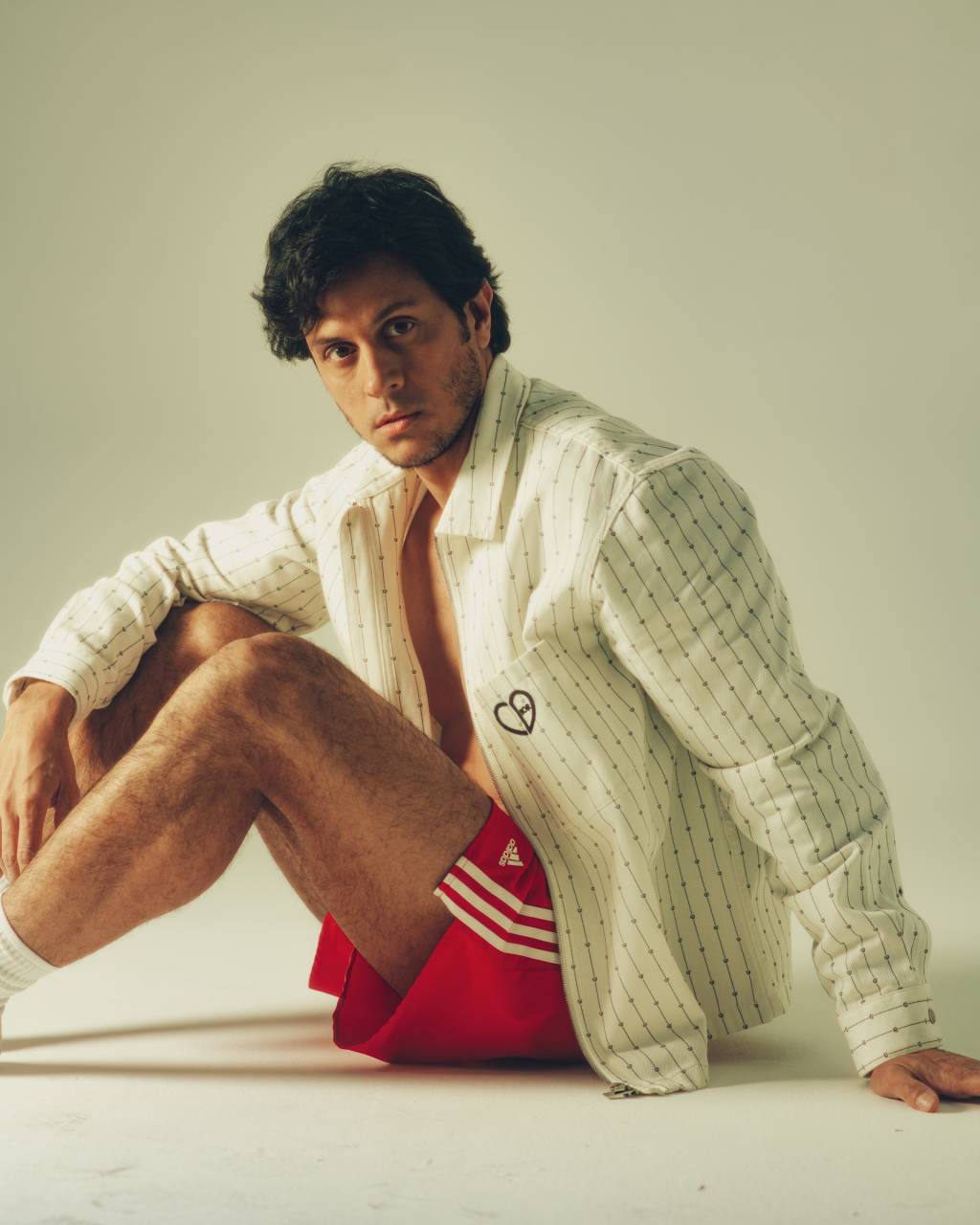 693_THIAGO MANSUR_180712 Homem sentado no chão de lado com jaqueta branca e shorts vermelho