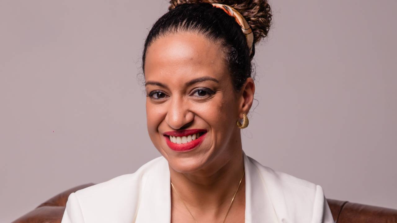 Mulher negra sorri e veste blazer branco com calça marrom