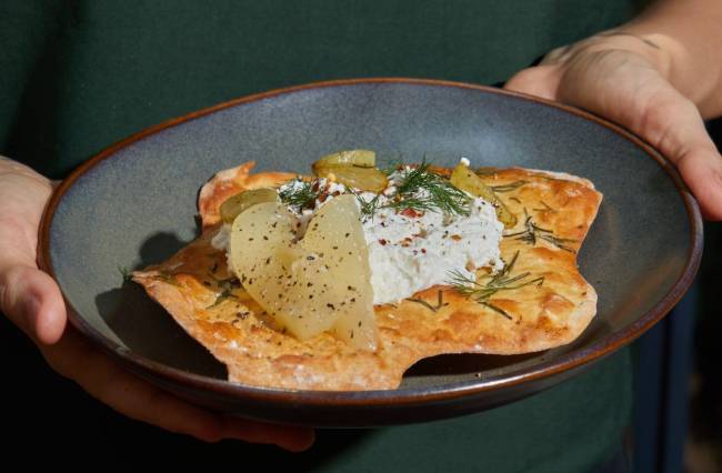 Prato azul com entrada com crostini e ricota com mãos segurando o prato