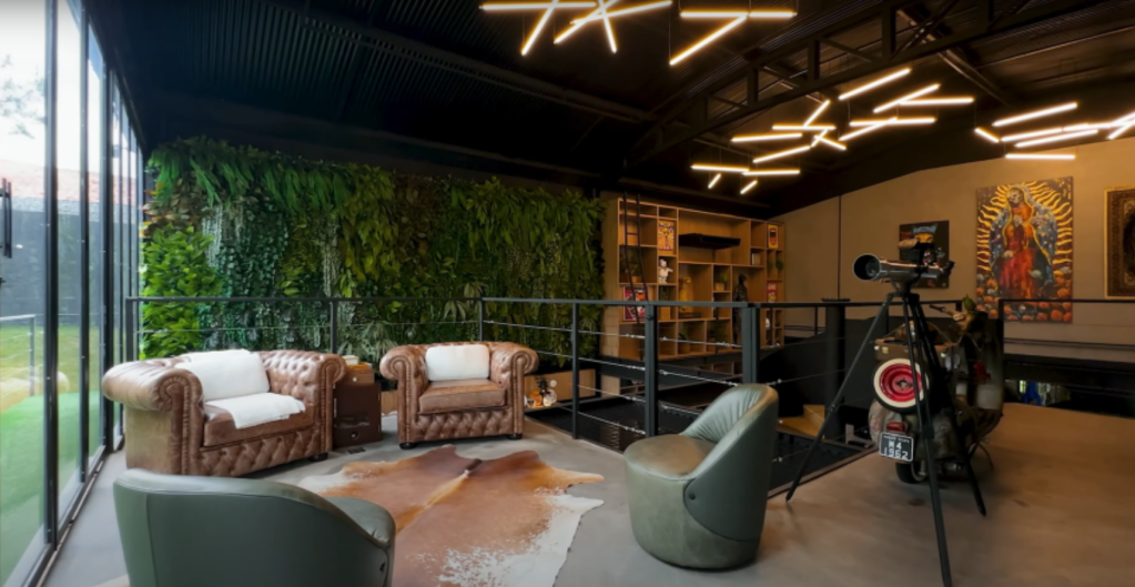 sala 1 segundo andar Sala de estar com poltrona verde moderna e sofás em tons claros. Ao fundo, parede esverdeada se assemelha a plantas suspensas