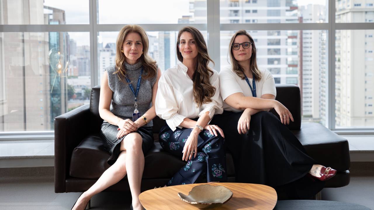 Três mulheres sentadas em frente a mesa de centro.