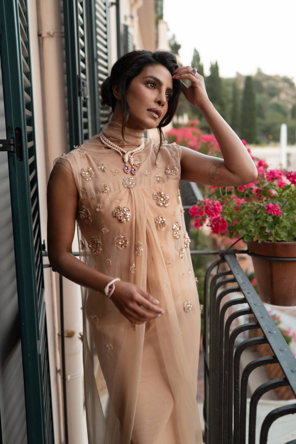 2025.05.19 Cannes – Bvlgari Priyanka Chopra F1002755 RT Priyanka Chopra em Taormina veste vestido bege e joias no pulso e pescoço, com jardim de fundo em varanda de hotel