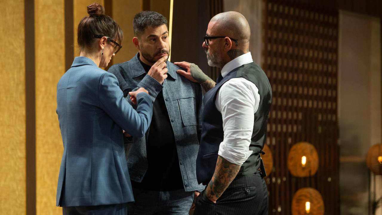 No cenário do MasterChef, estão três pessoas de pé: Helena Rizzo, Evaristo Costa e Henrique Fogaça