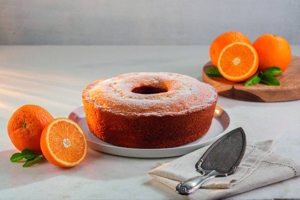 Bolo Tradicional de Laranja.jpg Bolo com laranjas em volta em prato branco