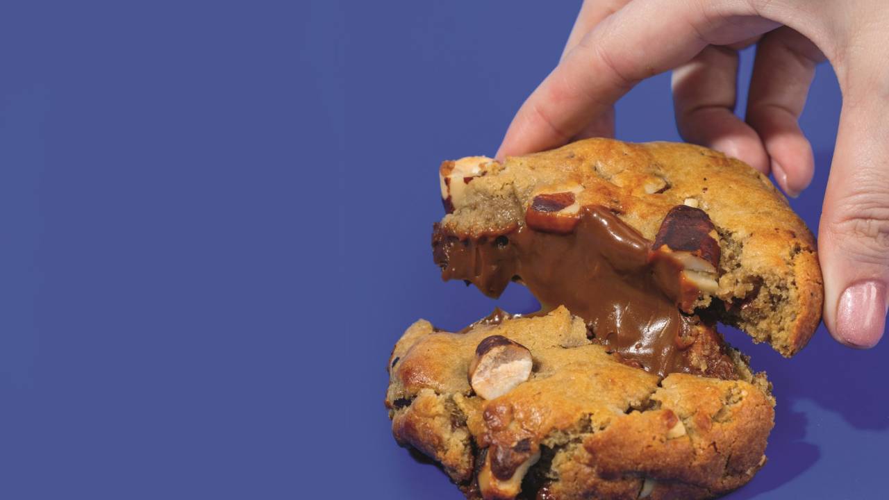 Mão segurando cookie com recheio de doce de leite e castanhas