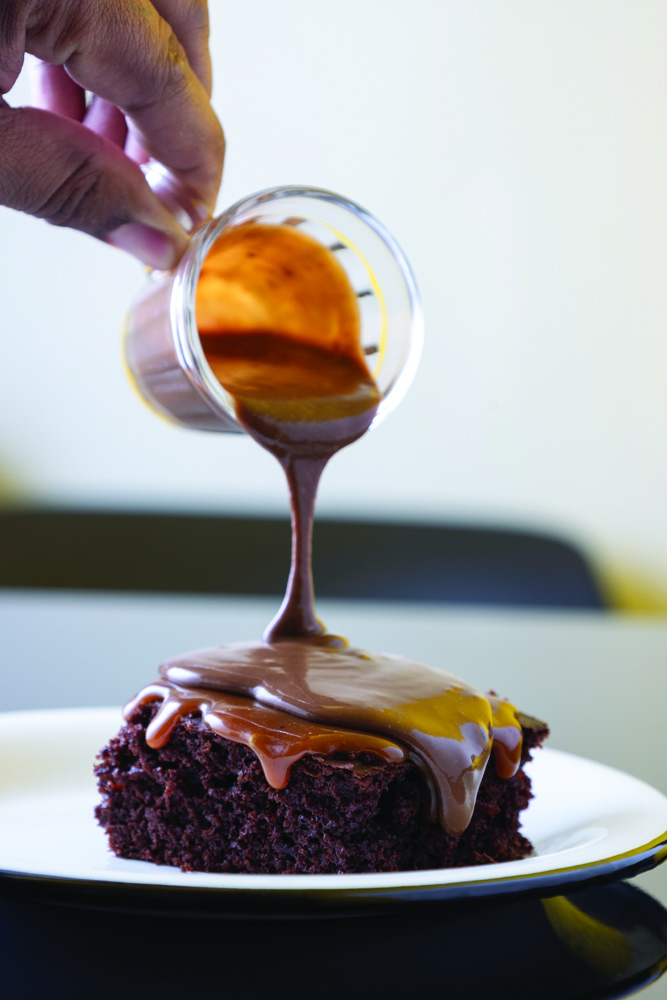 Bolo de chocolate com calda de caramelo salgado _ Matheus Rosa Confeitaria Bolo no prato com mão colocando calda no bolo