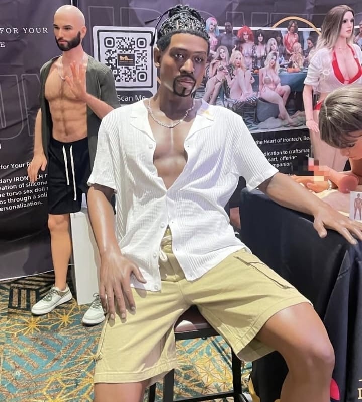 Namorado Reborn Crédito Exclusiva Sex-Reprodução (3) Boneco de homem negro sentado vestindo camisa branca e shorts bege em loja de produtos adultos
