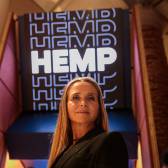 Mulher loira em frente a letreiro escrito HEMP