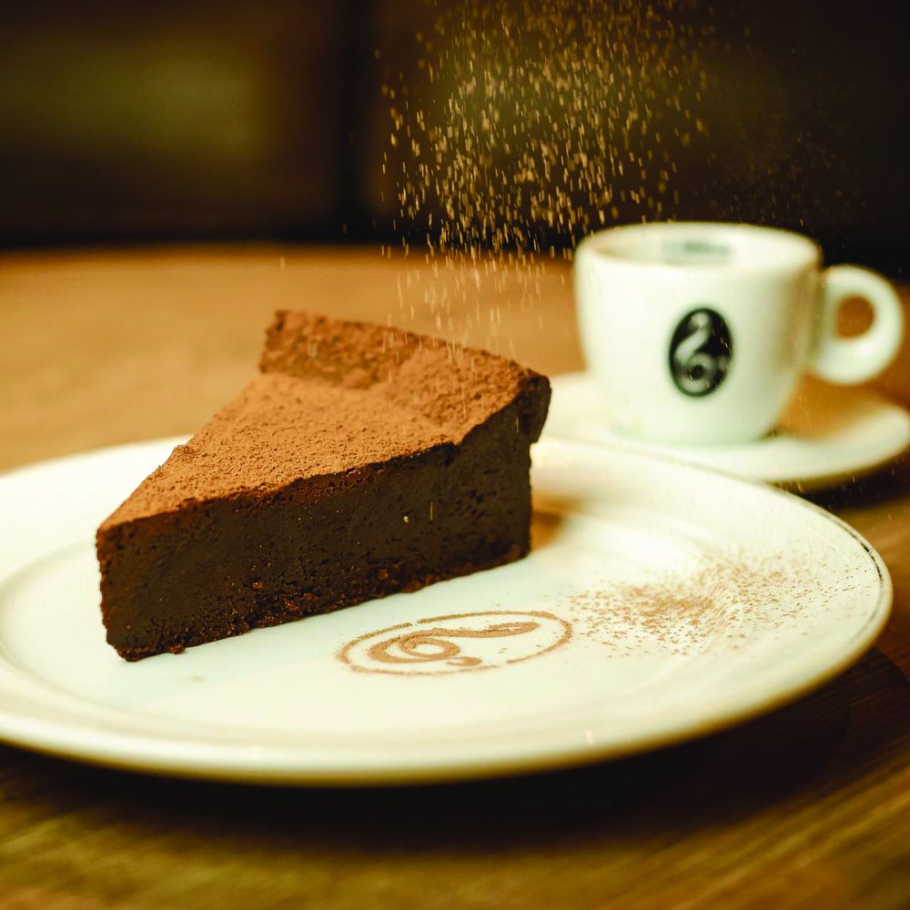 Torta de café – Il Barista.jpg Pedaço de torta em prato branco com café ao fundo