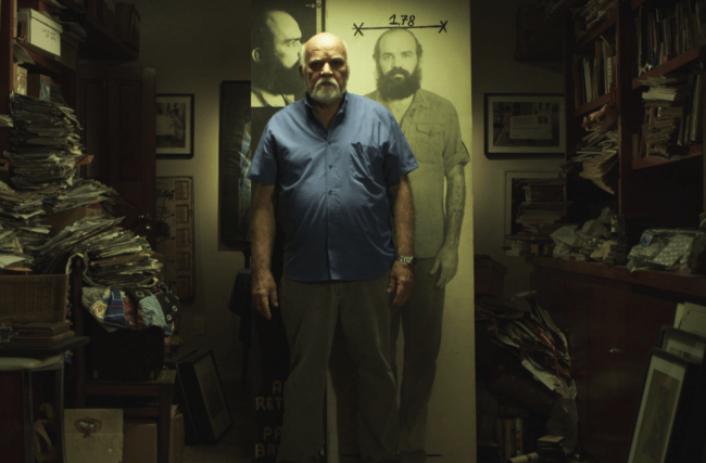 Paulo Bruscky Cortesia Galeria Nara Roesler_O artista em seu ateliê no Recife; atrás dele, sua obra Alto Retrato (1978), fotografia. paulo-bruscky-alto-retrato