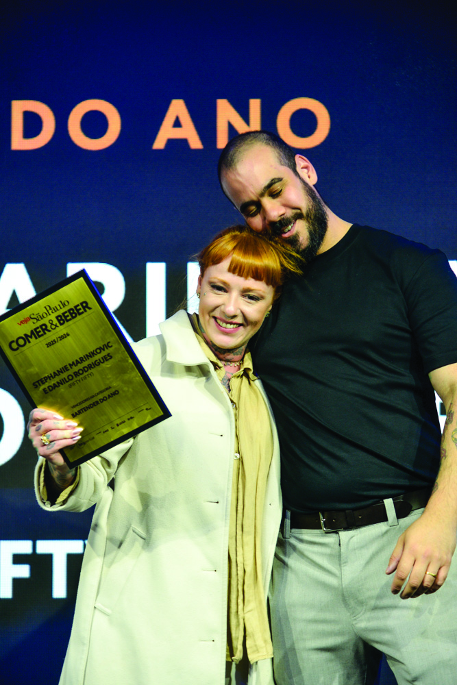 Casal abraçado e sorrindo com placa