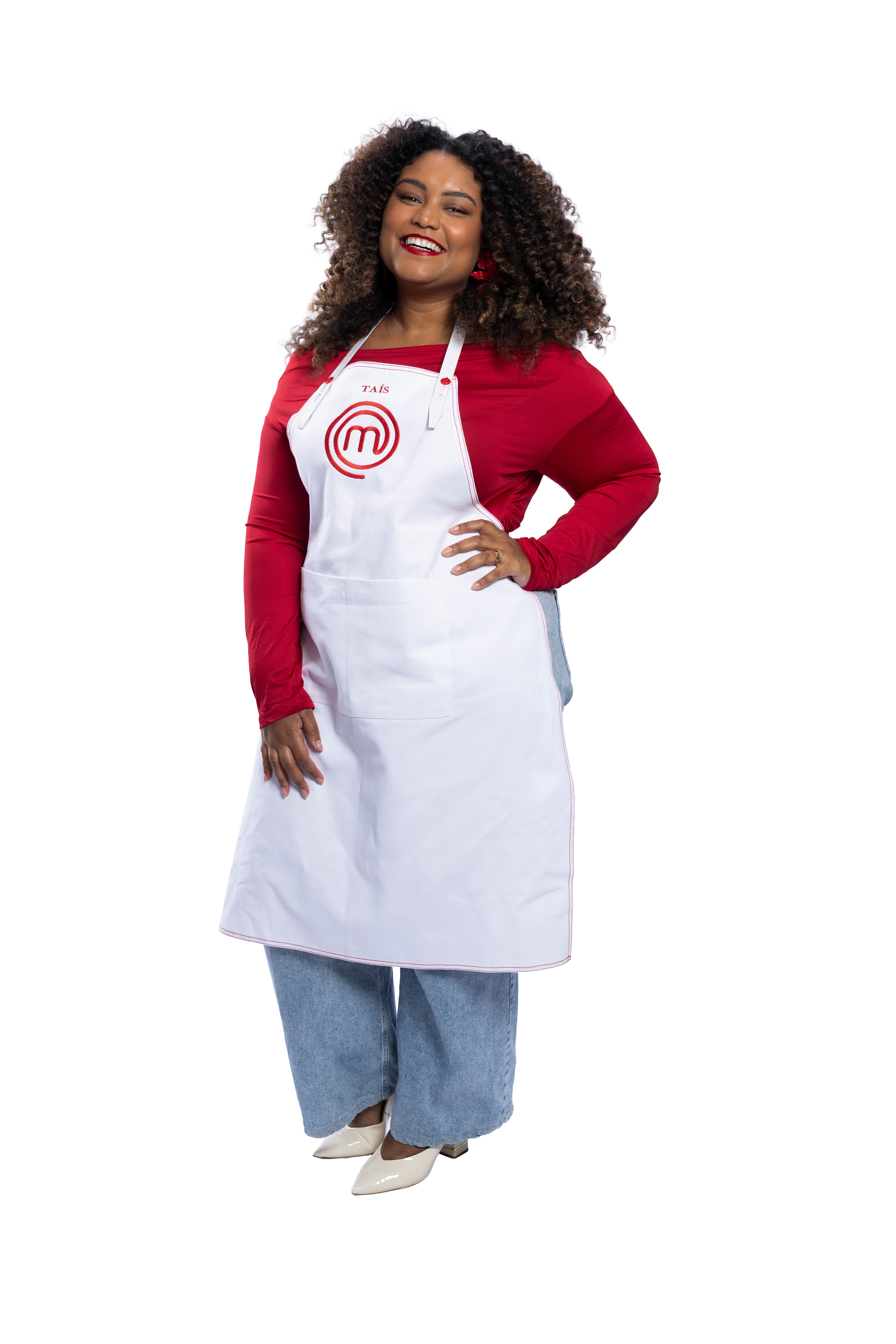 Mulher de pele escura e cabelos cacheados sorrindo, vestindo blusa vermelha, jeans e avental branco do MasterChef com seu nome 